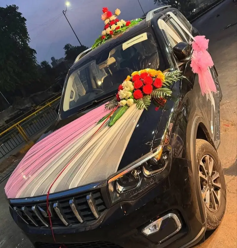 A car decorated with fresh flowers on the bonnet, a net drape down the windscreen and a pink bow on the mirror.