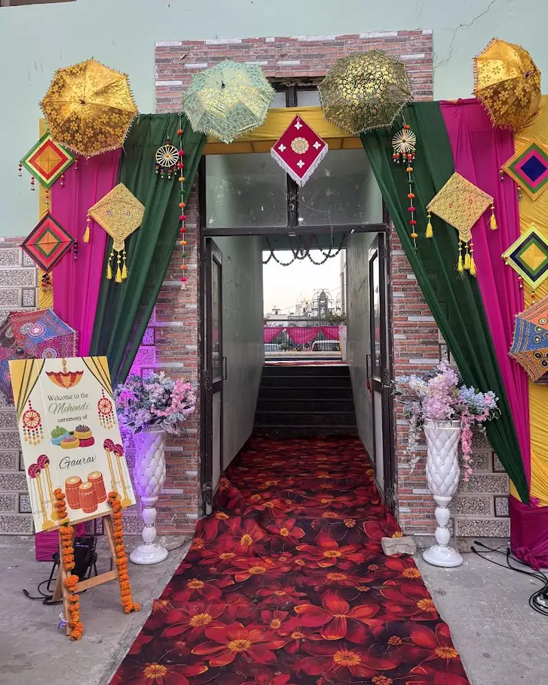 A hall entrance dressed with magenta and green drapes, hanging umbrellas and a red carpet leading in.