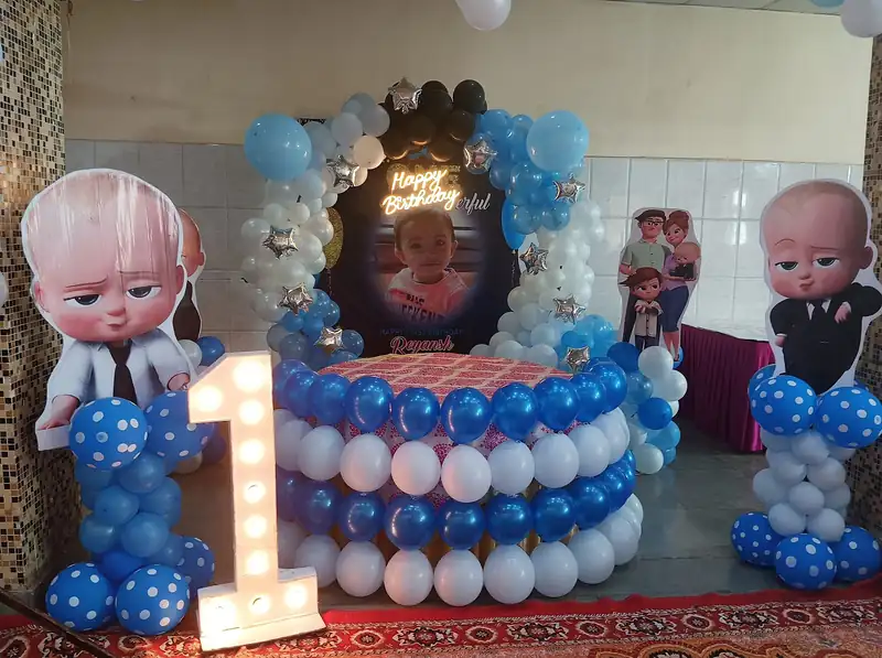 A first birthday setup in blue and white with cartoon cut-outs and a lit number one.