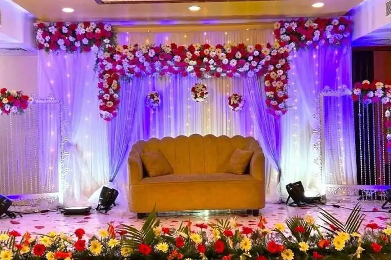 A reception stage with a gold sofa, a floral valance overhead and a bed of flowers along the front.