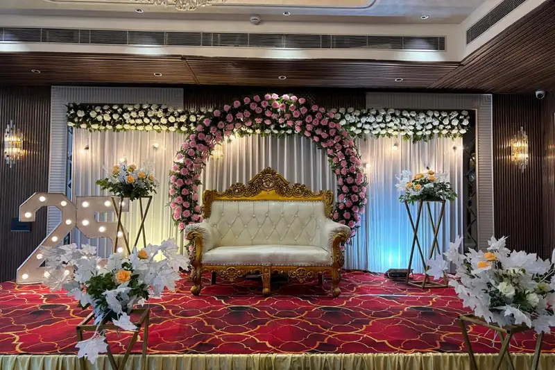 A banquet stage with a carved sofa inside a flower arch and lit standing letters at the side.