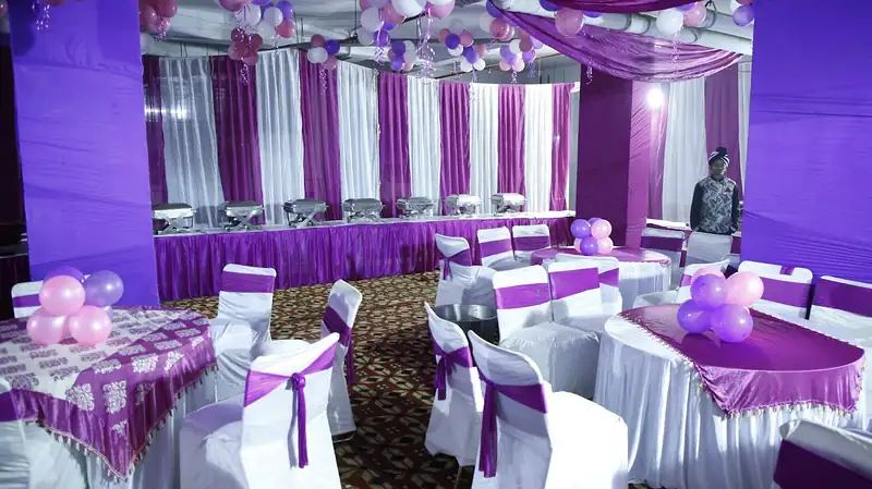 A banquet room laid with white chair covers, purple sashes and dressed tables.